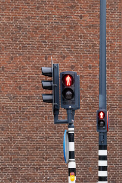 A close-up of a pedestrian traffic light showing the stop signal indicated by a red human icon, set against a background of a red brick wall, highlighting urban infrastructure.