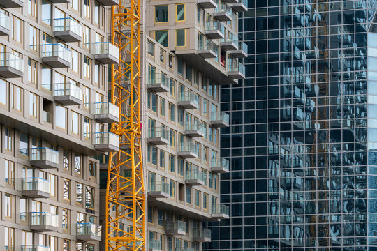 A construction site with a yellow crane positioned amidst modern buildings with reflective glass windows, depicting the ongoing urban development and growth within the cityscape setting.
