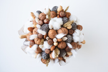 Beautiful handmade Christmas bouquet of nuts, pinecones and cotton flowers, top down view on white background. Holiday floral decor.