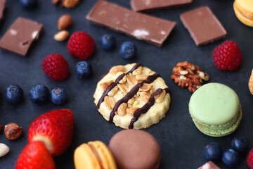 Macarons, chocolate, cookies, berries and various nuts on dark blue background. Selective focus.