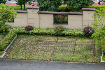 Elevated view of a grassy parking lot divided into several sections by rectangular patches, surrounded by landscaped plants and shrubs. The parking spaces are in a secured gated and fenced area.