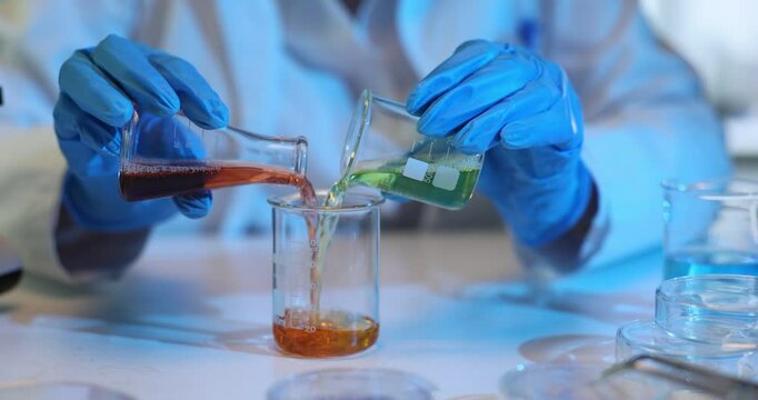 Scientist carefully mixes red and green liquids in glass demonstrating chemical reaction