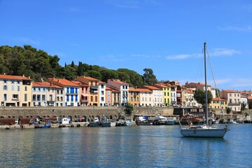 Sailboat in harbour against backdrop of colourful house fronts and blue sky in Mediterranean port town of Port-Vendres, Pyrénées-Orientales department, southern France 