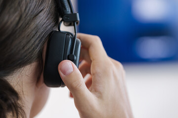 Close-up view of teenage boy puts on wireless headphones and connect them to tv for watching movie. Turn on device
