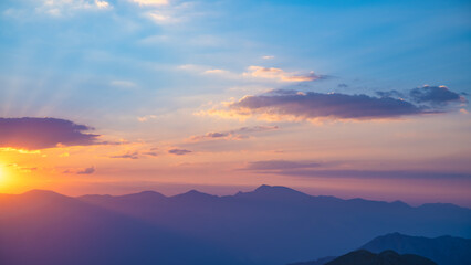 Obraz premium The setting sun over the mountains, the beautiful sun's rays shine through the clouds, the natural background, freedom, tranquility and peace