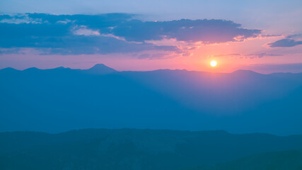 Obraz premium The setting sun over the mountains, the beautiful sun's rays shine through the clouds, the natural background, freedom, tranquility and peace