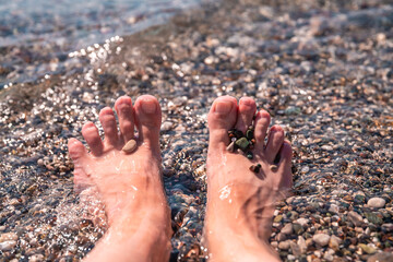 close up Female feet on the background of the sea surf, on the beach with small pebbles, concept vacation at the sea, relax