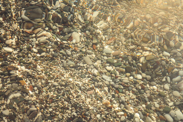 multi-colored stones under water on the sea, river. Natural background of stones, glare on the water