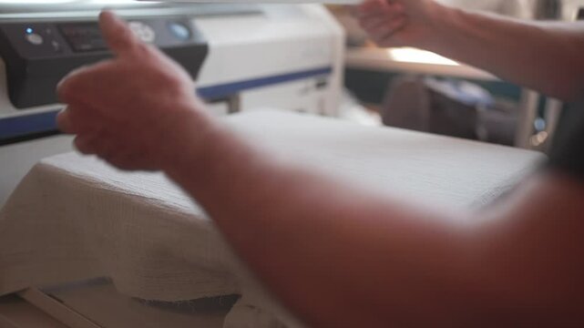 Person placing fabric material on square holder and attaching frame around material. Getting ready to use press. Printed logo on clothing. Completing embroidery with help of modern machinery.