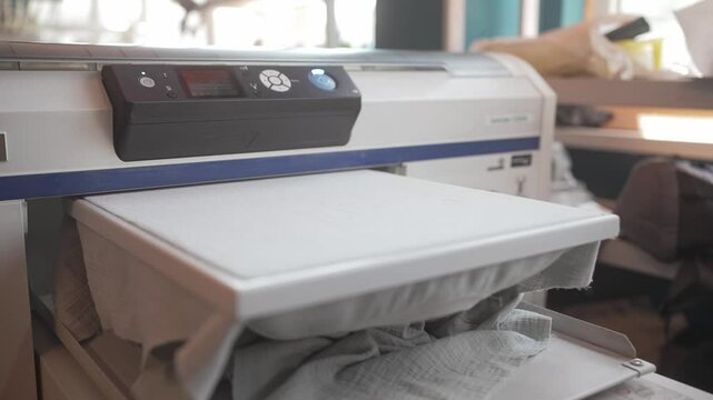 Person pressing buttons on modern heat press. Square surface with frame sliding into machine. Creating logo or sign on shirt or other clothing. Completing embroidery. Fashion concept.
