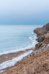 Mystical winter storm on the shore of a frozen sea with rocky shores. Winter frozen sea and snowstorm. Winter sea fairy tale.