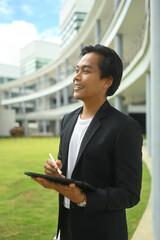 Confident asian businessman holding digital tablet and looking away while standing outdoor