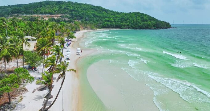 Drone aerial view in Vietnam flying over Phu Quoc island Sao beach, white sand, crystal clear blue turquoise water, green palm trees and people walking on a sunny day