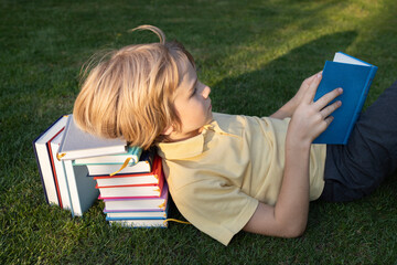 child lies on grass with his head on a stack of books and reads one. Get involved in reading, back...