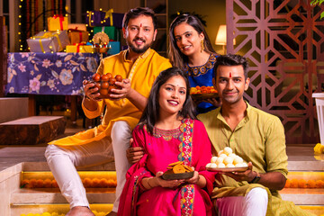 Cheerful Indian couples and friends celebrating Diwali at home with drinks, sweets, taking selfies