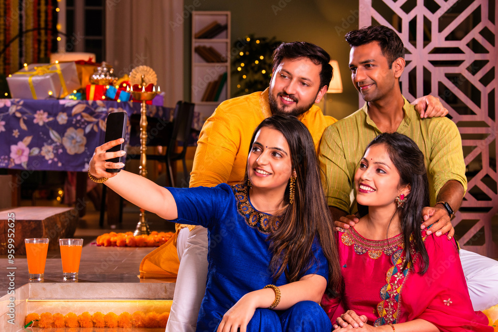 Wall mural Cheerful Indian couples and friends celebrating Diwali at home with drinks, sweets, taking selfies