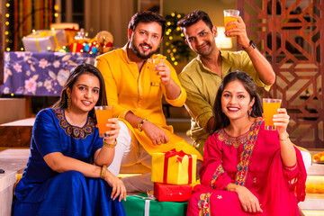 Cheerful Indian couples and friends celebrating Diwali at home with drinks, sweets, taking selfies