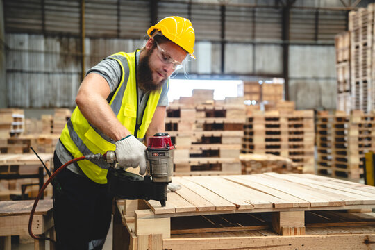 A man in a yellow vest is using a nail gun to attach wood to a pallet