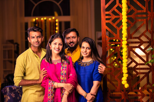 Happy Indian couples and friends standing in traditional dress, celebrating Diwali festival at home - Powered by Adobe
