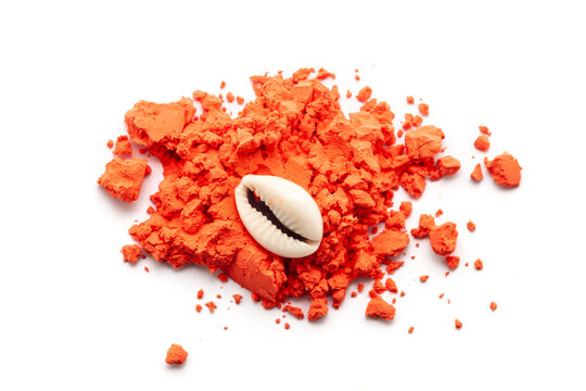 Top view of Cowrie (Cypraea chinensis) placed over a pile of orange-colored sindoor (vermilion), isolated on a white background.