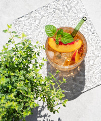 Peach lemonade with ice and mint on a concrete background. Fresh iced tea in a glass with shadow and herb.