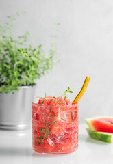Refreshing watermelon cocktail in glass with thyme and ice on a light background with fresh herbs and fruits.