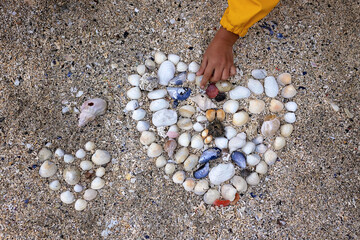 Beautiful blond child, boy, gathering shells on a beach in Norway, making heart