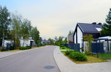 Prefab house. Street in residential area. Contemporary Residence in suburb. Rows of modern houses along road. Family house, Modern Home outside city. Trees, green lawn at Villa. Modern barnhouse.