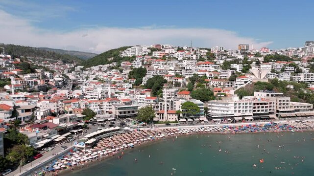 Flying backwards revealing the busy touristy beach and bay of Ulcinj with its white house, landscape abd blue adriatic sea water