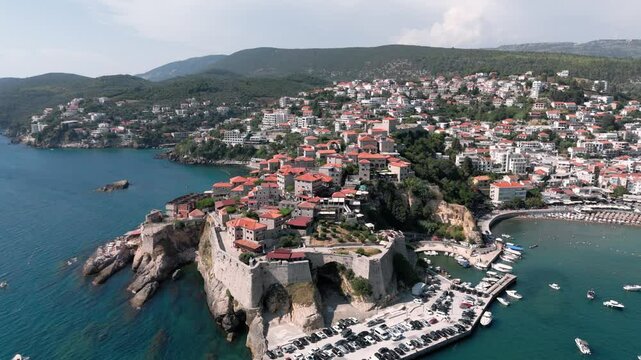 Flying around the fortress of Ulcinj revealing the busy touristy beach and bay with its white houses, landscape and blue adriatic sea water