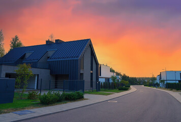 Obraz premium Barn House in village on sunset. Modern luxury house in suburb. Street with Wooden Scandi home. Modern Scandinavian Barnhouse Project. Contemporary barnhouse. Rows of Barn Houses along road village.
