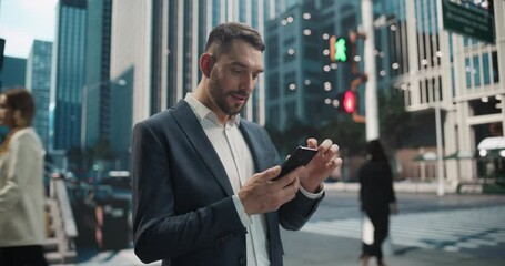 Happy Caucasian Man in a Suit Uses His Smartphone on a Bustling City Street, Surrounded by Modern Skyscrapers and Pedestrians. He is Using Apps, Reviewing Documents and Preparing Notes for a Meeting 