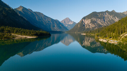 Tranquil reflections of mountains and trees in Plansee, Austria during a clear sunny day