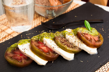 Caprese salad with mozzarella, black tomatoes and pesto on black stone plate