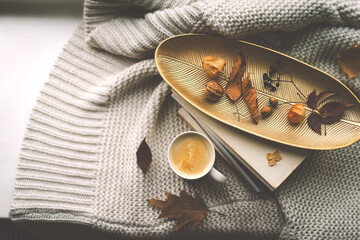 A warm cup of coffee sits atop a golden tray adorned with dried leaves, resting on a stack of...
