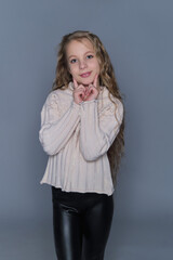 A young girl with long, wavy hair gently rests her hands on her cheeks, wearing a cozy knit sweater. This image emphasizes natural beauty and children's winter fashion, showcasing warmth and comfort.