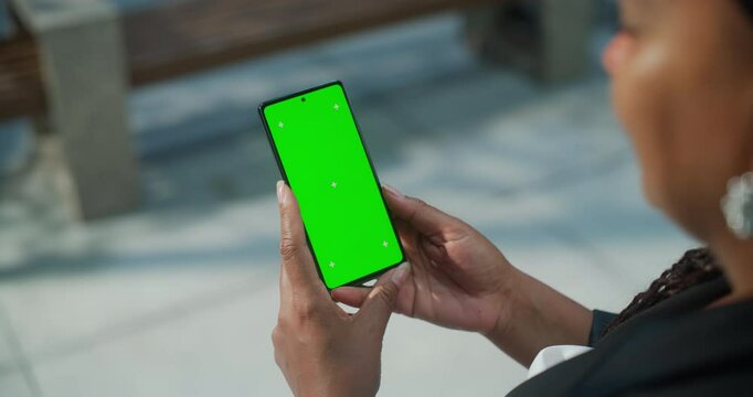 Female Holding a Green Screen Mock Up Chroma Key Smartphone on a Street. Over the Shoulder Footage of a Person Using a  Mobile Phone. Template for Internet, Social Media, Online Shopping App