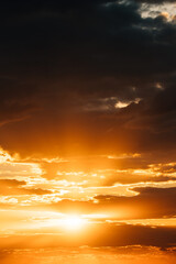 Natural Bright Dramatic Sky In Sunset Dawn Sunrise. Amazing Bold Golden Sunset Sunrise Sky Background. Warm Yellow And Orange Colors. Dark Clouds with Sun