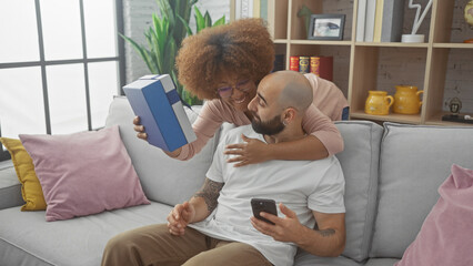 Interracial couple enjoys a cozy moment with a gift and smartphone on a comfortable sofa at home