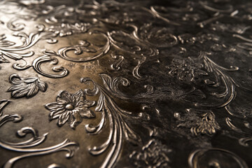 A bronze textured surface featuring intricate, engraved patterns that create a sense of elegance and craftsmanship, with a slightly weathered finish.