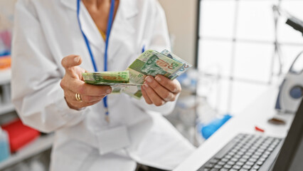 A woman in a lab coat counts hong kong dollars inside a laboratory, with a blurry computer and...