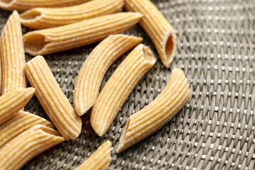 Uncooked organic penne quinoa pasta on a textured braided rustic cloth. Unique raw natural ingredients for gluten free diet 