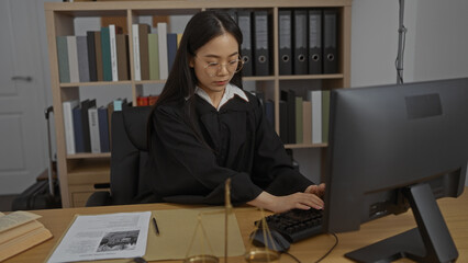 Woman working in an office, wearing judicial robes, typing at a desk with legal documents and scales of justice, interior setting with bookshelves and binders in the background