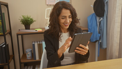 A smiling middle-aged woman using a tablet in a modern home office setup.