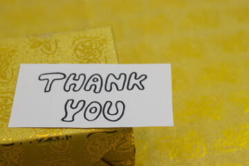 Thank you hand written notes with golden gift box in background.