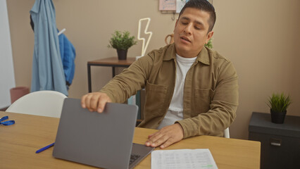 Hispanic man closing laptop in modern home office with casual jacket and indoor plants.