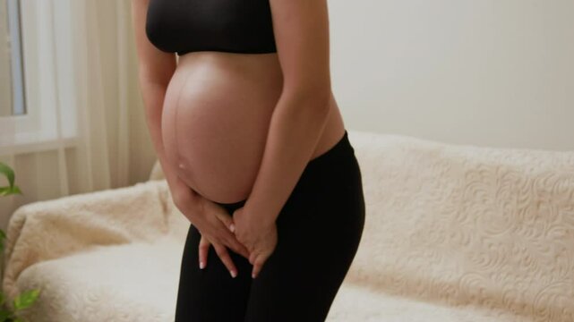 Incontinence and frequent urination during pregnancy. The young pregnant woman with a sports figure holds her hands between her legs, wanting to urinate. Concept of pregnancy and its periods