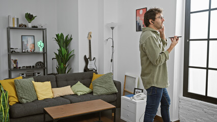 Hispanic man speaks handsfree in modern living room with guitar and cozy sofa.