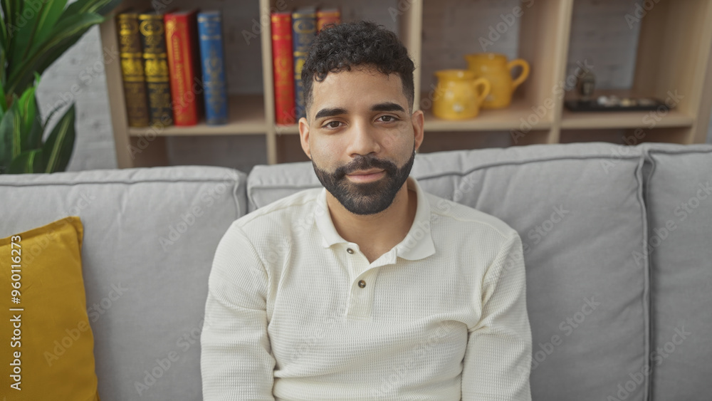 Sticker A young hispanic man with a beard, sitting on a couch in a cozy living room, exuding a casual and handsome appearance.