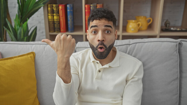 Surprised hispanic man with beard gesturing in a modern living room.